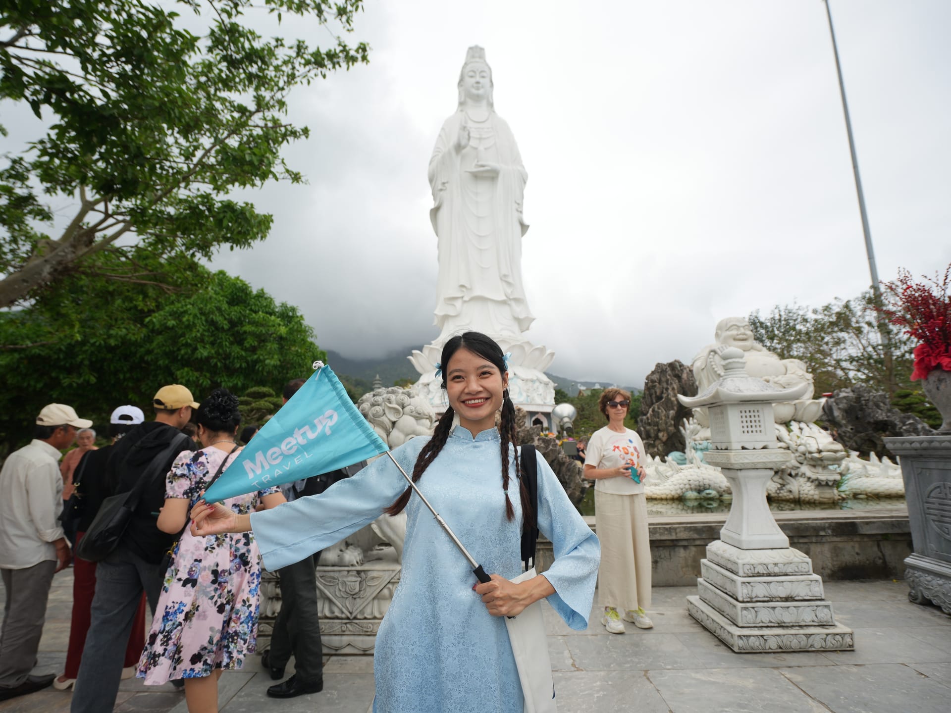 Meetup tour guide wearing light blue ao dai in front of Lady Buddha statue at Linh Ung Pagoda in Da Nang, Vietnam.