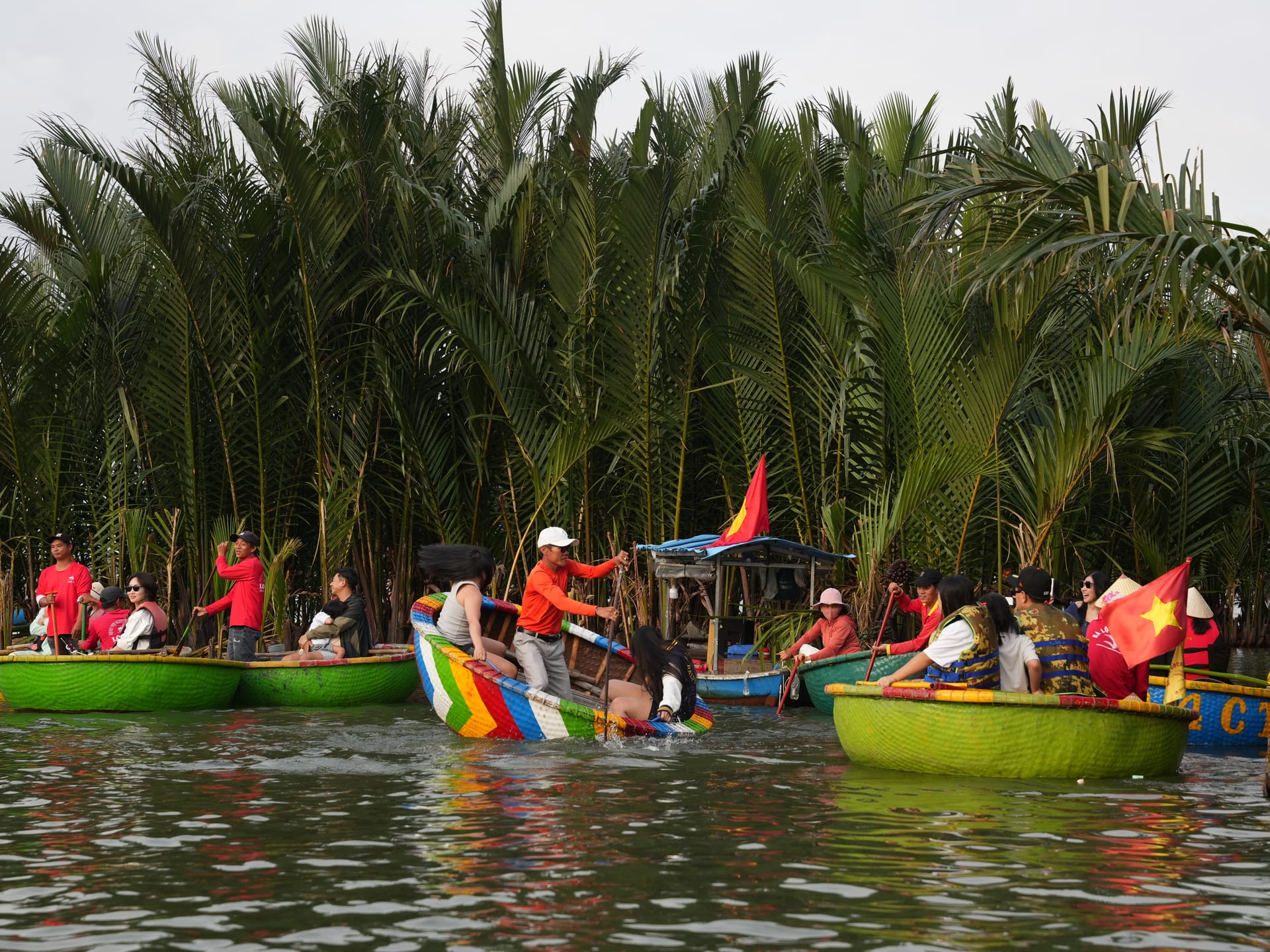 Tourists riding colorful bamboo basket boats in Bay Mau Coconut Forest in Hoi An, Vietnam.