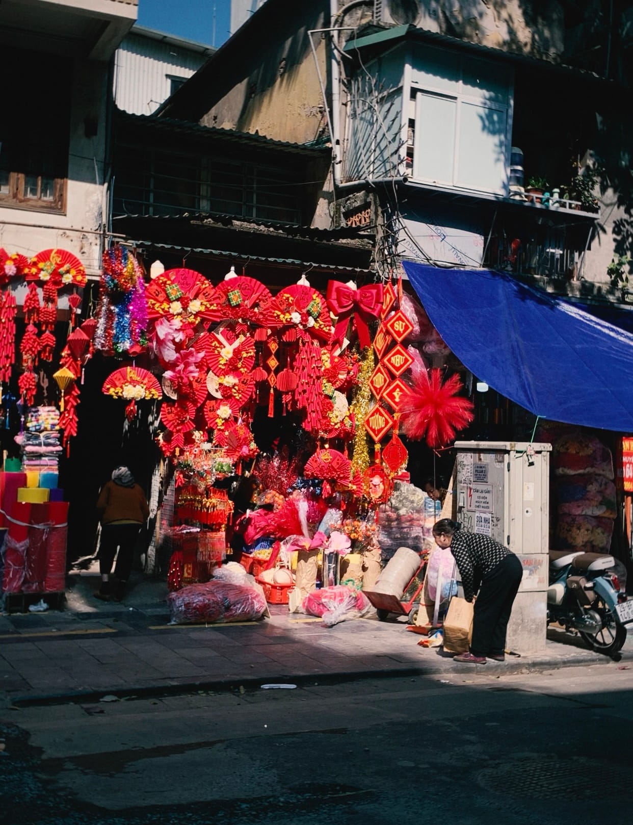 Crowded market lane in Hanoi's Old Quarter with vendor stalls and goods on both sides.