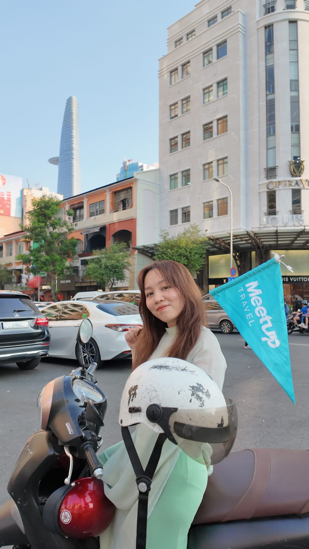 Meetup Travel guide holding a company flag beside a motorbike in central Ho Chi Minh City
