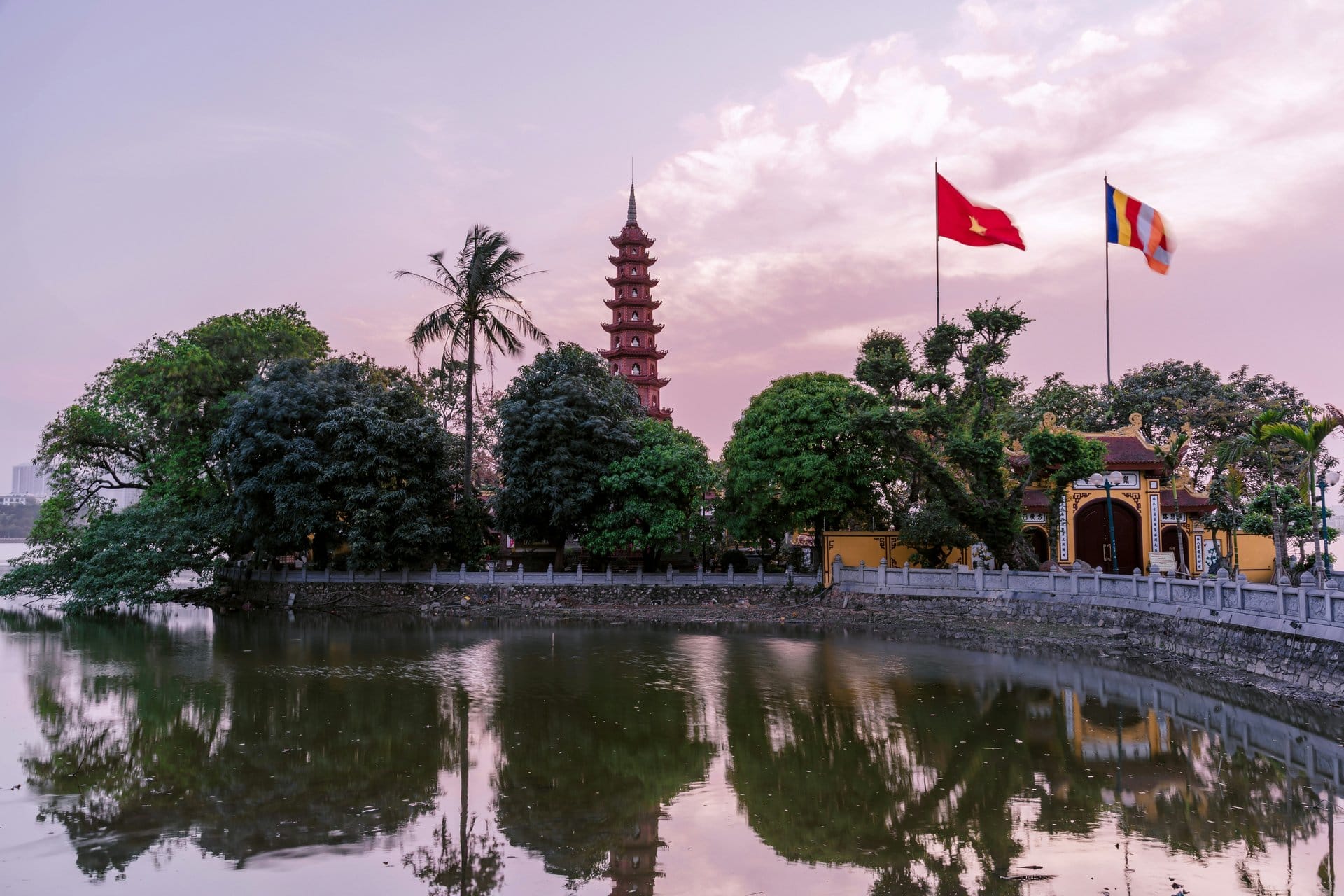 Tran Quoc Pagoda's tiered brick tower glows at sunset, mirrored in the still water of West Lake.