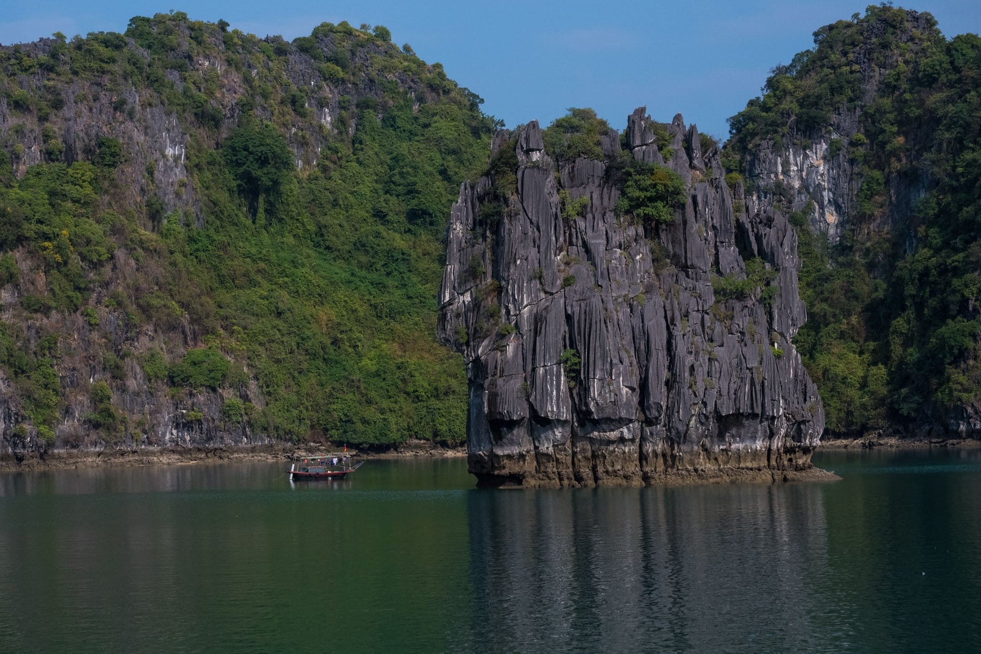 Sunrise light glows orange behind rows of limestone karst islands rising from calm water.