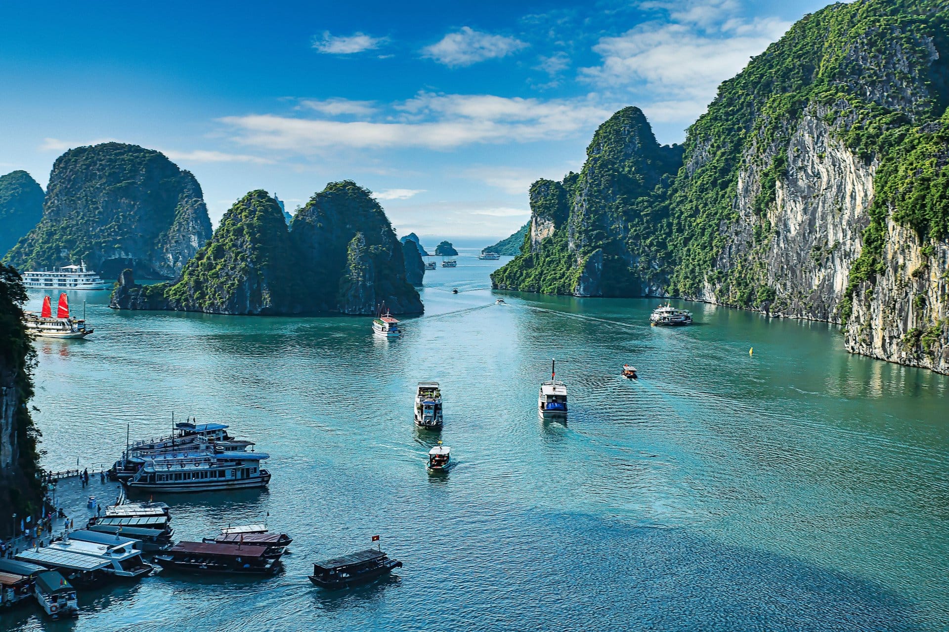 Two kayakers paddle through a narrow rock archway into a shaded, enclosed lagoon.