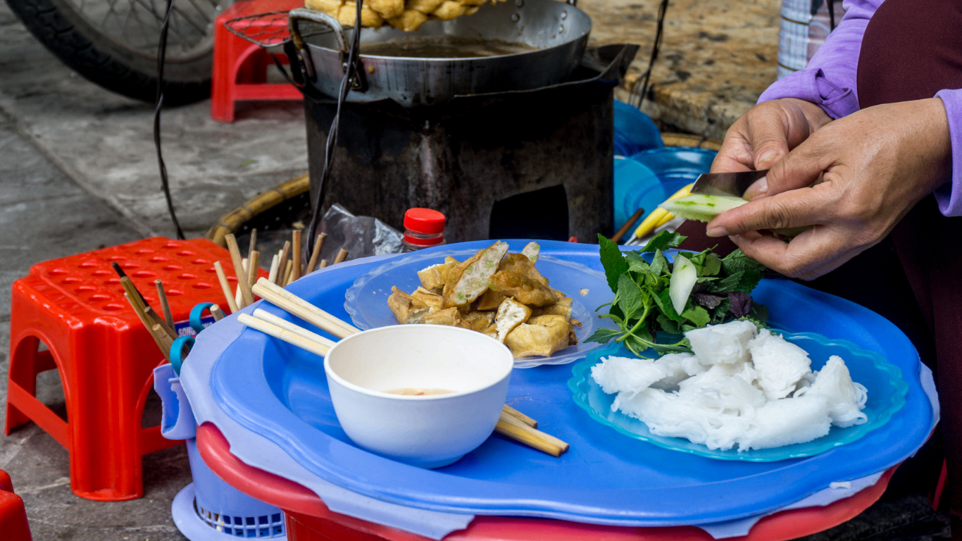 Vietnamese street food vendor ladling broth at a sidewalk stall with pots of soup on a gas burner