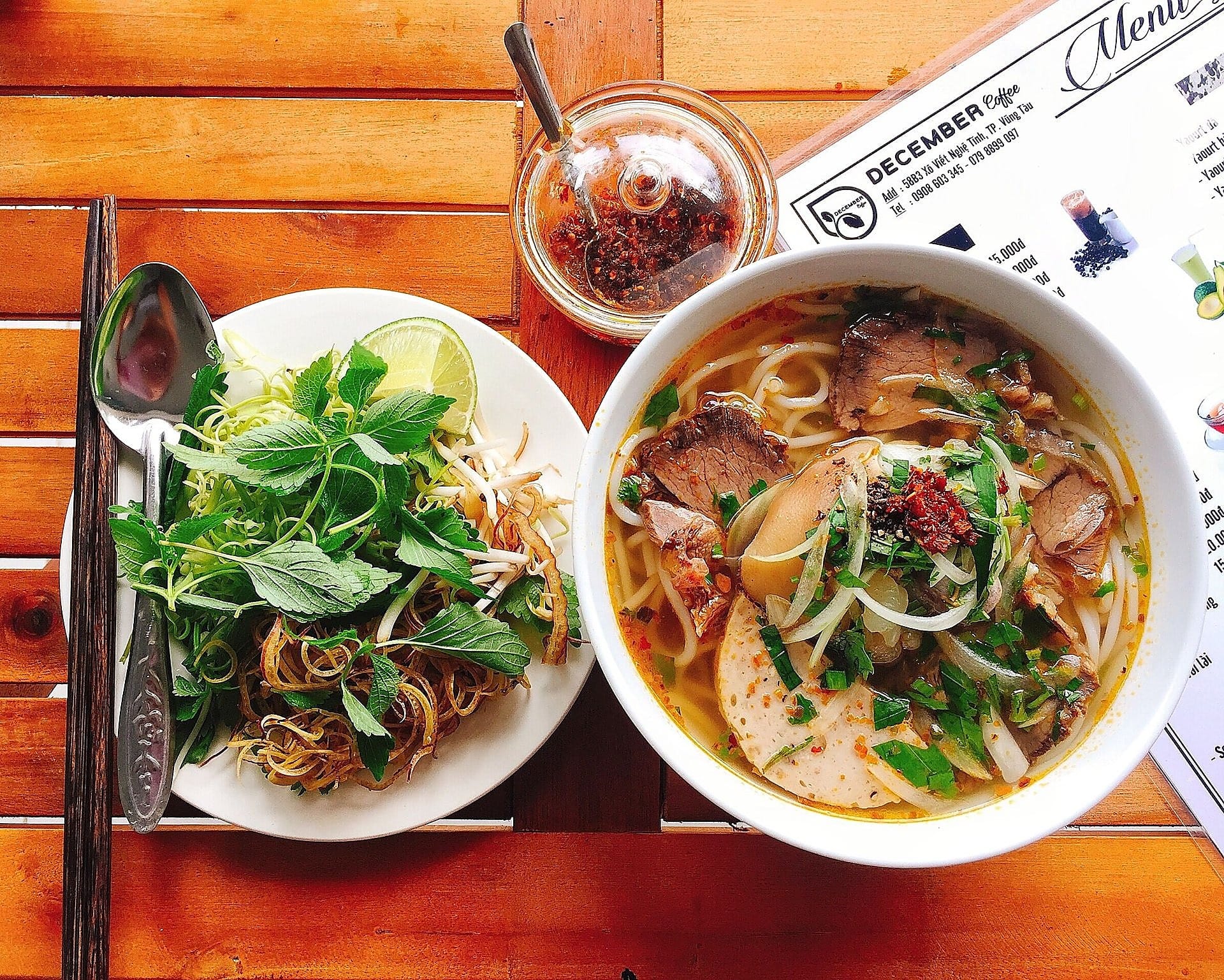 Bowl of Vietnamese noodle soup with meat slices, fresh herbs, lime and chilli oil