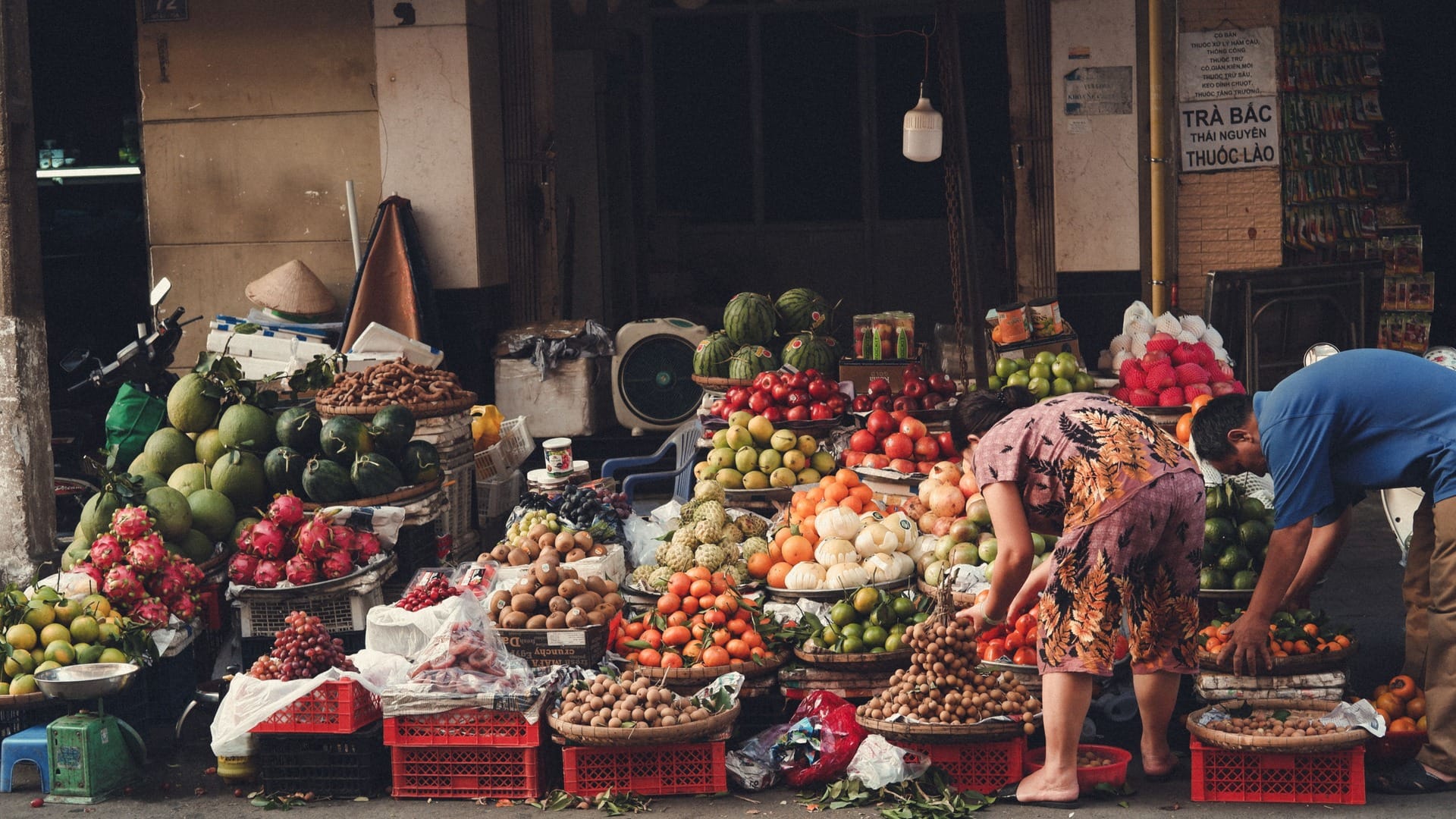 A vendor ladles broth into bowls at a pho stall while bones and herbs simmer nearby