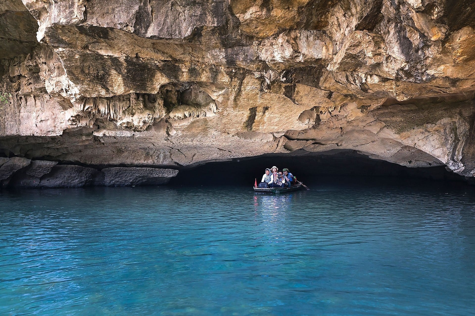 Traditional sampan boat pass under a natural karst cave ceiling on the river tour.