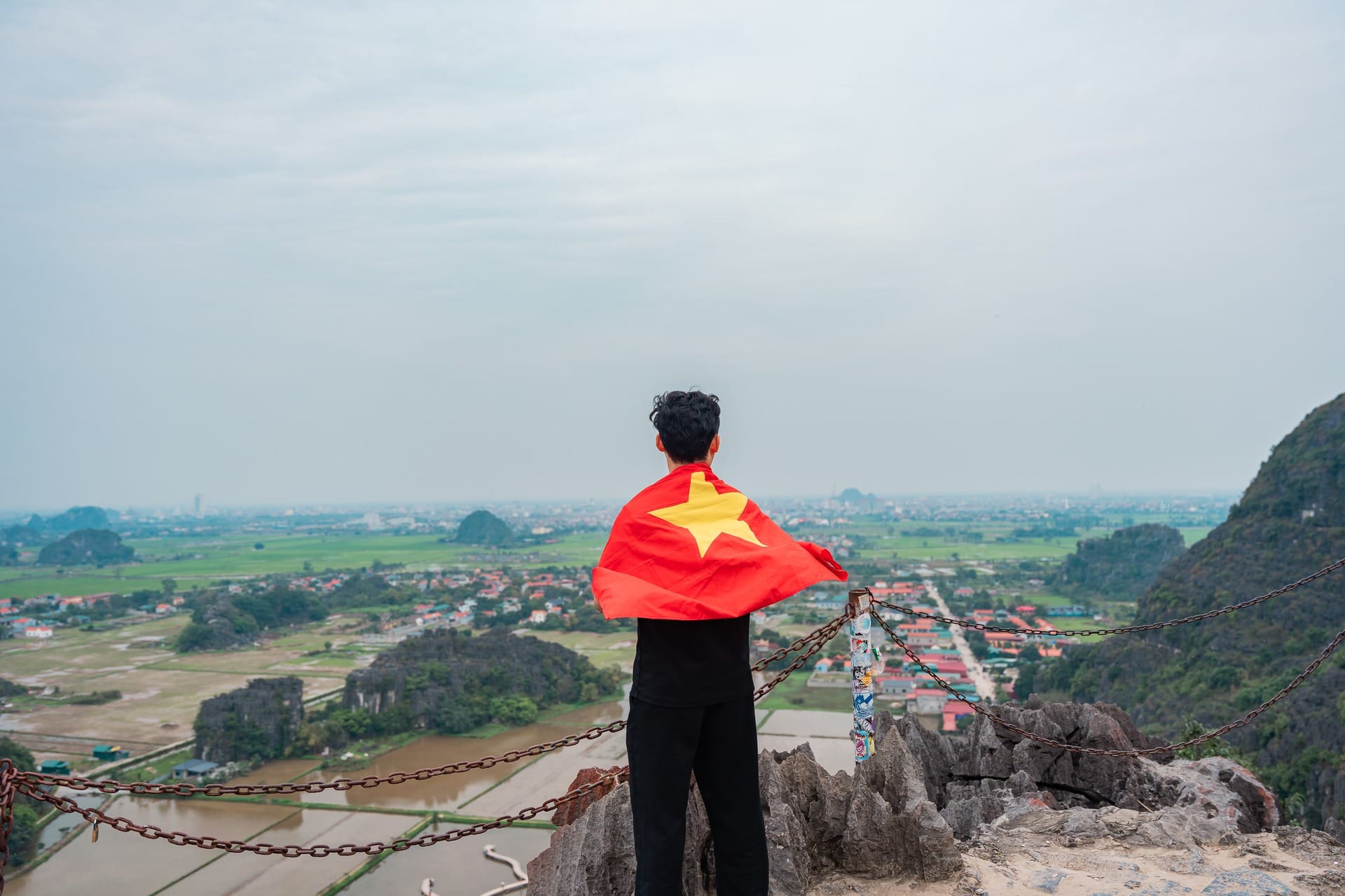 Wide valley view of rice fields and limestone hills seen from a hillside trail in Ninh Binh