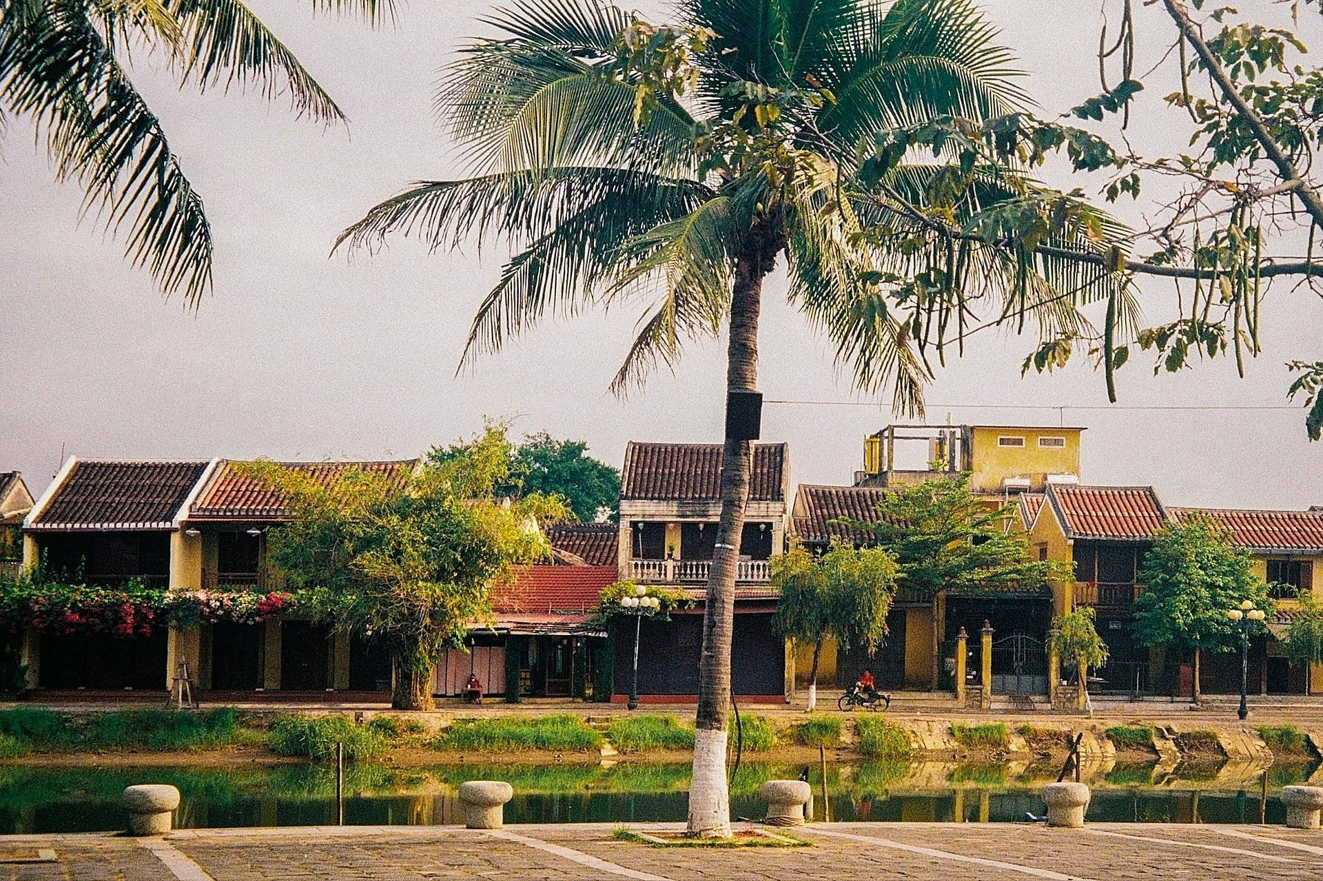 Wooden covered bridge with a tiled roof arching over a narrow canal in Hoi An's Old Quarter.