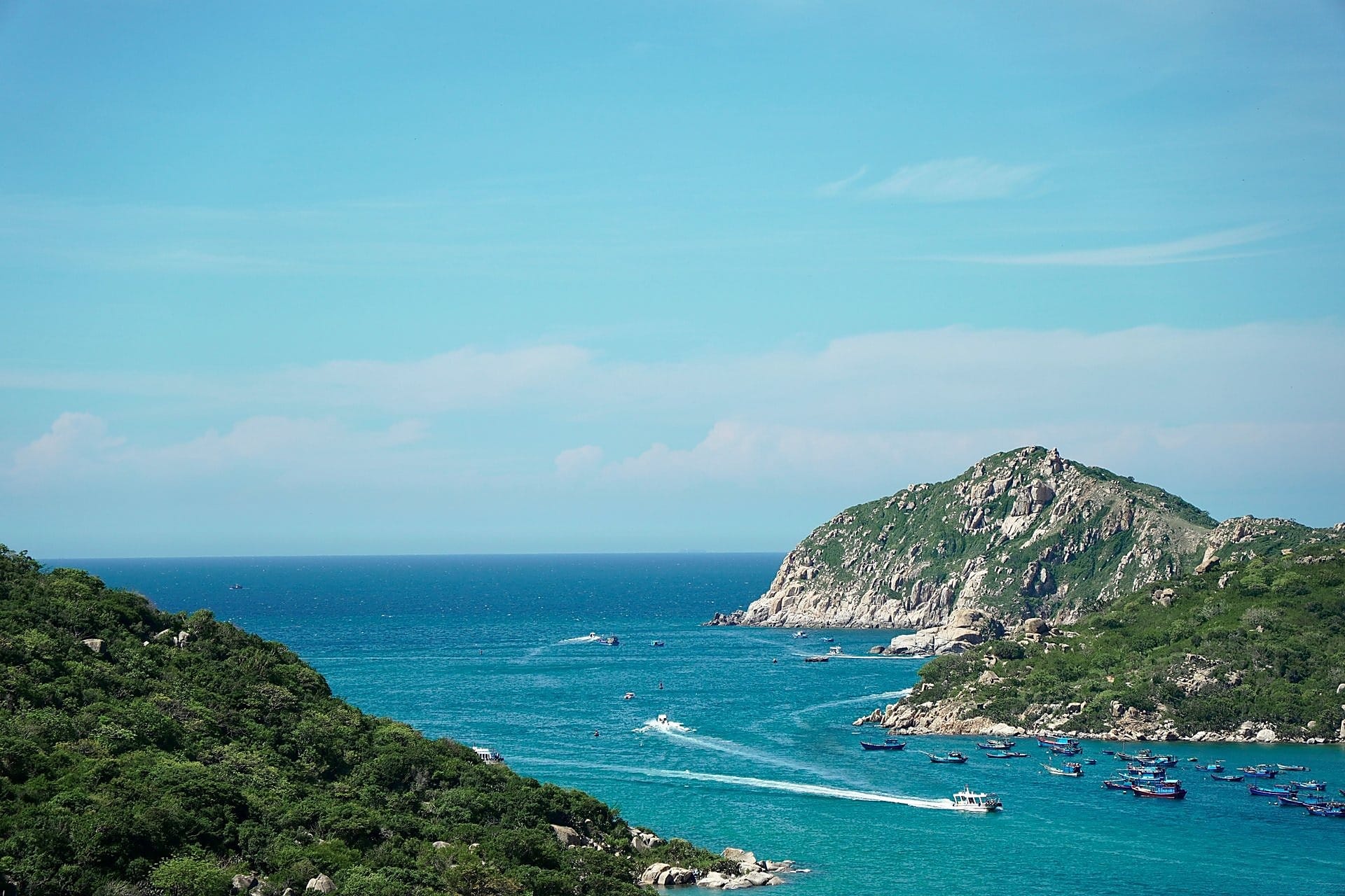 Scenic coastal view of green hills meeting turquoise sea with speedboats in Con Dao Vietnam