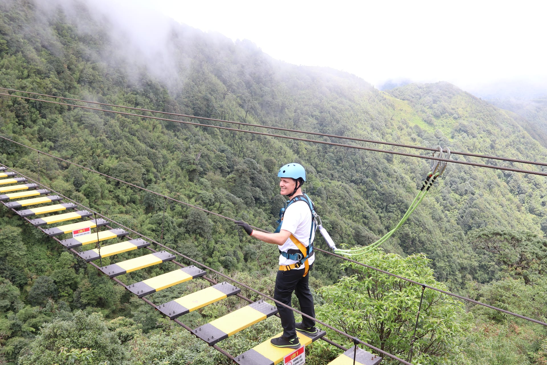 Meetup Travel customer crossing a hanging bridge walkway in misty mountains during a Sa Pa tour.