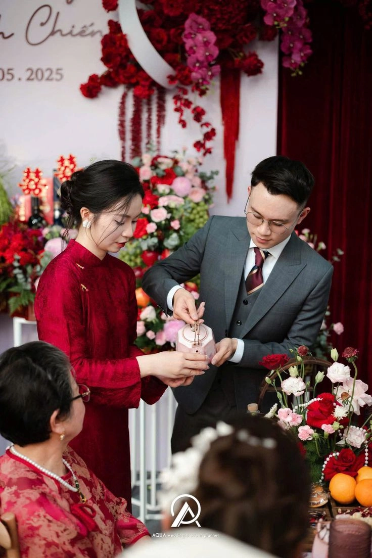 Vietnamese bride and groom in traditional ao dai standing at their engagement ceremony surrounded by family.