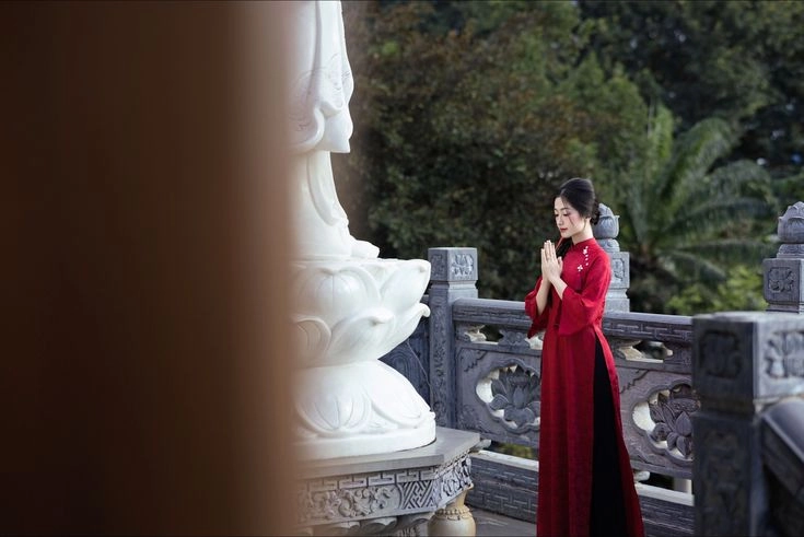 Vietnamese woman praying in front of a white Buddha statue at a Buddhist temple in Vietnam.