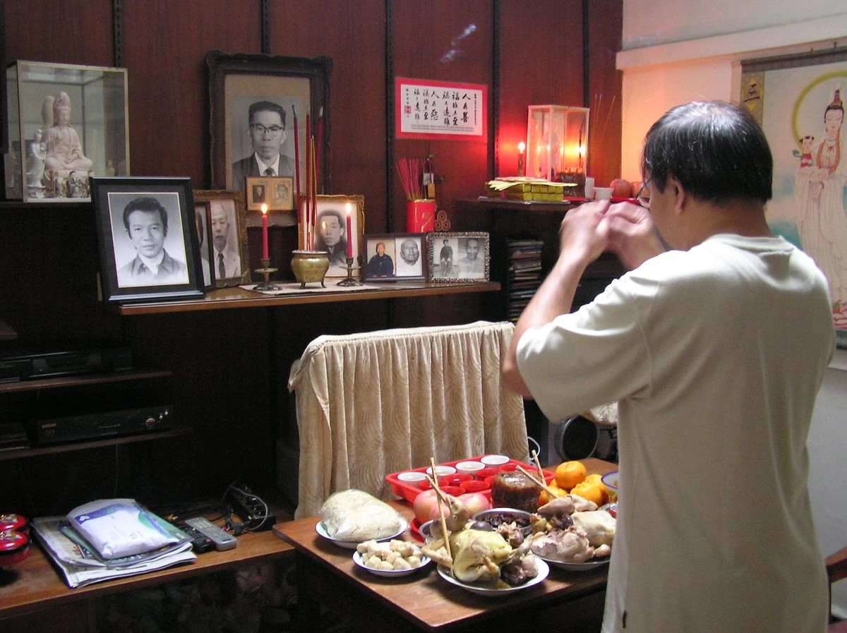 Vietnamese man praying in front of a traditional family ancestor altar at home.